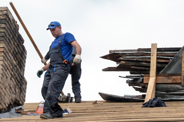 Réparation d'un vieux toit en bois Charpentier avec des outils sur le toit contre le ciel Un travailleur professionnel dans un uniforme de protection travaille à la hauteur d'une maison délabrée