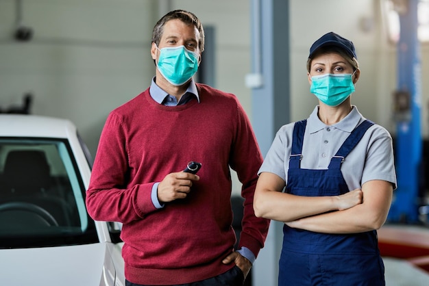 Réparatrice automobile et son client masculin avec des masques de protection debout dans un atelier et regardant la caméra