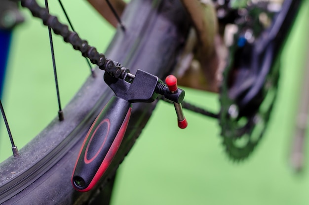 Réparer un vélo de montagne dans l'atelier Remplacement d'une vieille chaîne rouillée par une nouvelle Outil pour faire le retrait et l'installation de la chaîne en gros plan Fond vert