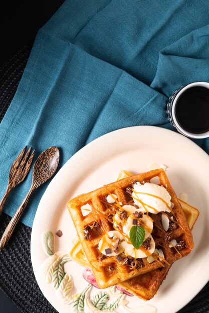 Repas alimentaire Concept de petit-déjeuner Gaufres bio maison garniture de glace vanille banane avec sauce caramel sur fond noir with copy space