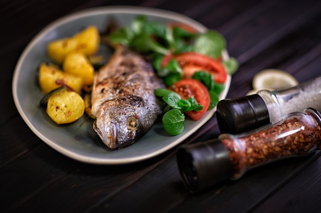 Photo repas poisson dorado au four avec des légumes au four sur un fond sombre.