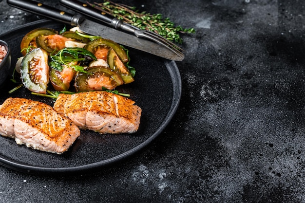 Repas de poisson avec steaks de filet de saumon rôti et salade de tomates roquette sur une assiette. Fond noir. Vue de dessus. Espace de copie.