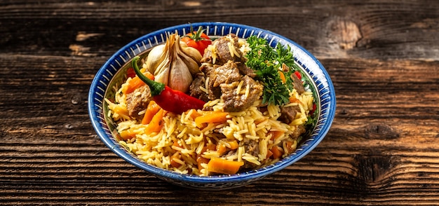 Repas traditionnel ouzbek appelé pilaf. Riz à la viande, la carotte et l'oignon en assiette avec ornement oriental, fond en bois, concept de cuisine orientale ouzbek.