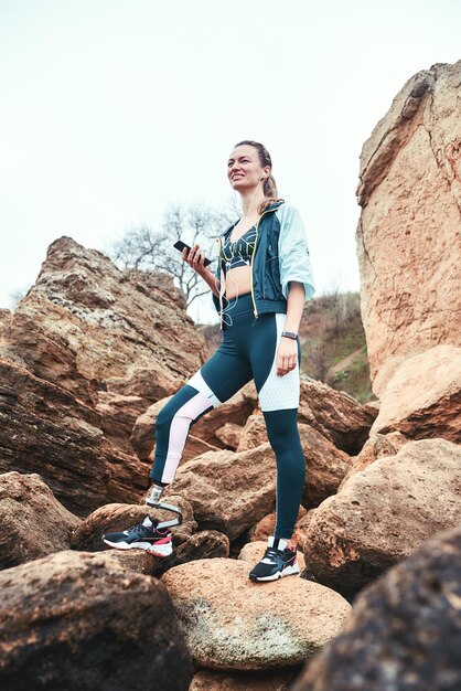 Repos après entraînement femme handicapée en tenue de sport avec prothèse de jambe tenant un téléphone dans elle