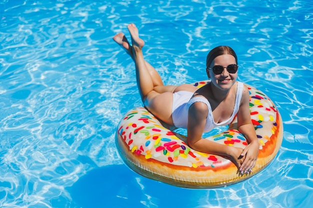 Repos dans la piscine Heureuse jeune femme en maillot de bain lunettes de soleil et anneau en caoutchouc gonflable flottant dans l'eau bleue Vacances de luxe d'été dans la piscine de la station thermale