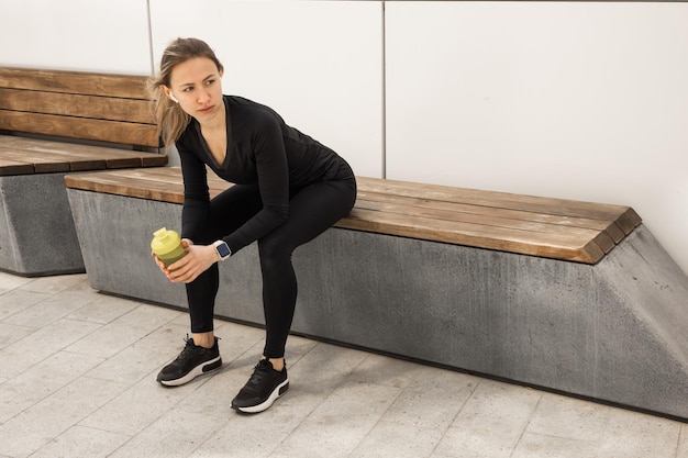 reposant sur un banc une jeune femme en survêtement noir avec un shaker