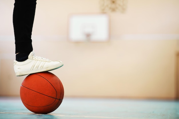 Un repose-pied humain sur le basket-ball sur sol en béton. Photo d'un ballon de basket et d'espadrilles dans un plancher en bois.