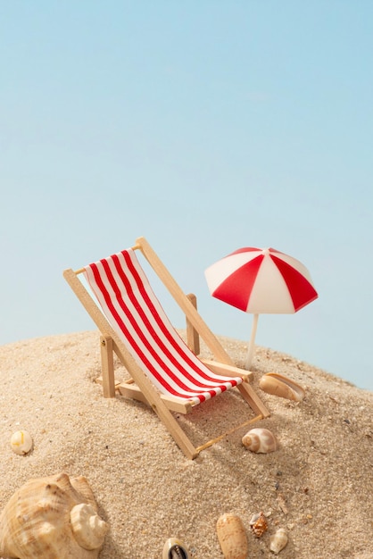Reposez une chaise de plage rouge miniature sur le sable avec des coquillages