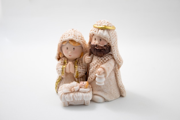 Représentation d'une crèche de Noël avec les figures de l'enfant Jésus, Marie et Joseph sur fond blanc.