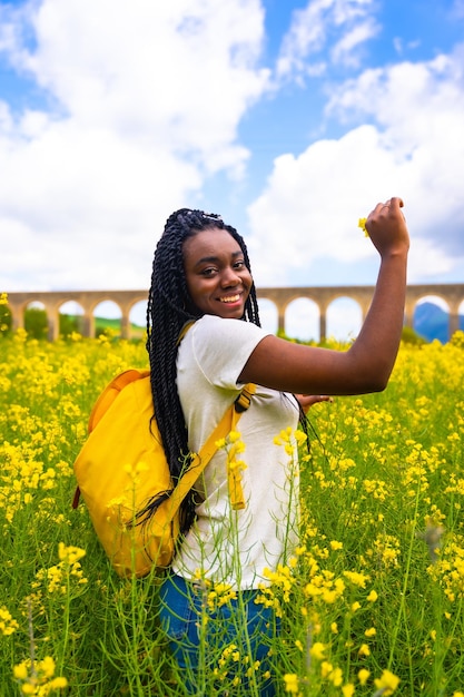 Respirer l'air frais et le parfum de la fleur une fille ethnique noire avec des tresses un voyageur dans un champ de fleurs jaunes