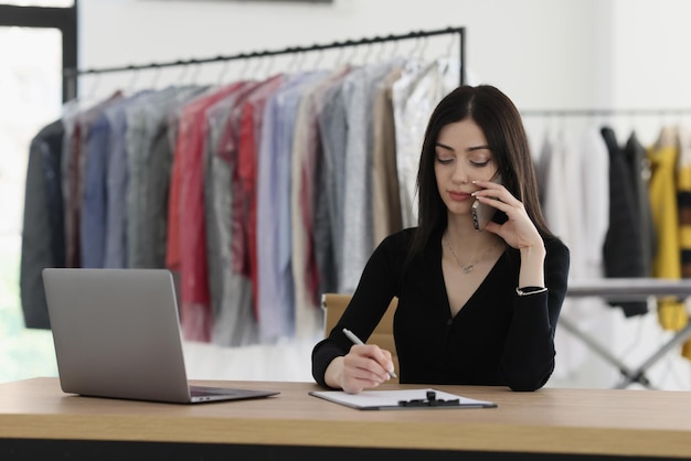 Le responsable du point de nettoyage à sec parle au téléphone en prenant des notes une personne de sexe féminin résout les tâches de travail