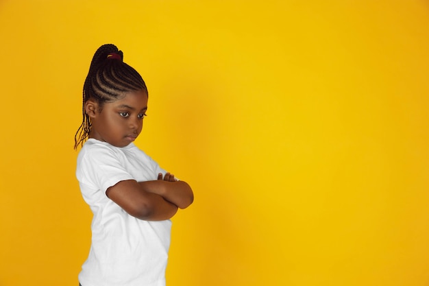 Ressentiment, rancune, tristesse. Portrait de petite fille afro-américaine sur fond de studio jaune. Gai, beau gosse. Concept d'émotions humaines, d'expression, de vente, d'annonce. Espace de copie. Ça a l'air mignon.