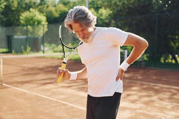 Ressentir de la douleur à cause d'un traumatisme Senior homme élégant et moderne à l'extérieur sur le terrain de sport pendant la journée