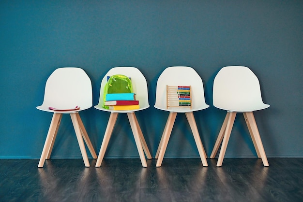 Ressources pour l'apprentissage Prise de vue en studio d'une rangée de chaises avec des livres et d'autres supports d'apprentissage sur un fond bleu