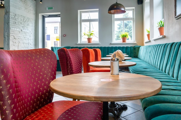 Un restaurant confortable et moderne avec des chaises rembourrées colorées et des canapés confortables Conception de café inhabituelle avec des murs en béton brut et des poutres décoratives en bois au plafond