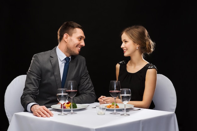 restaurant, couple et concept de vacances - couple souriant mangeant un plat principal avec du vin rouge au restaurant