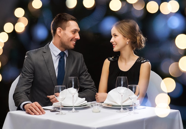 restaurant, couple et concept de vacances - couple souriant se regardant au restaurant