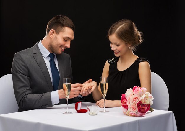 restaurant, couple et concept de vacances - homme souriant mettant une bague de fiançailles au restaurant