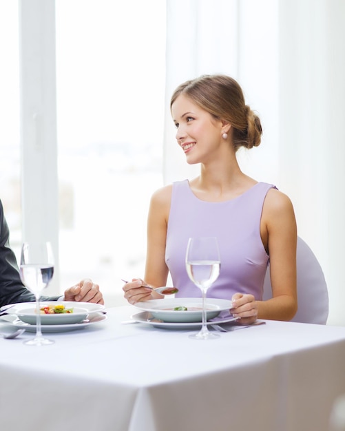 restaurant, couple et concept de vacances - jeune femme souriante regardant son mari ou son petit ami tout en mangeant un premier plat au restaurant