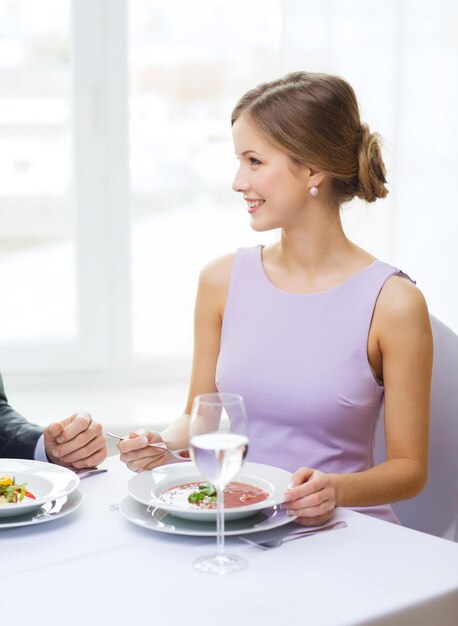 restaurant, couple et concept de vacances - jeune femme souriante regardant son mari ou son petit ami tout en mangeant un premier plat au restaurant