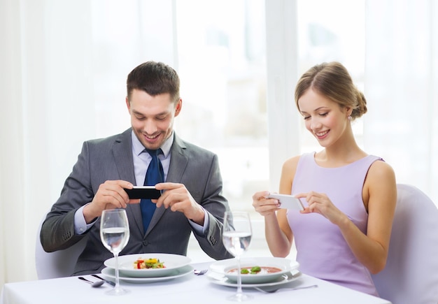 restaurant, couple, technologie et concept de vacances - couple souriant prenant une photo de l'apéritif avec l'appareil photo du smartphone au restaurant