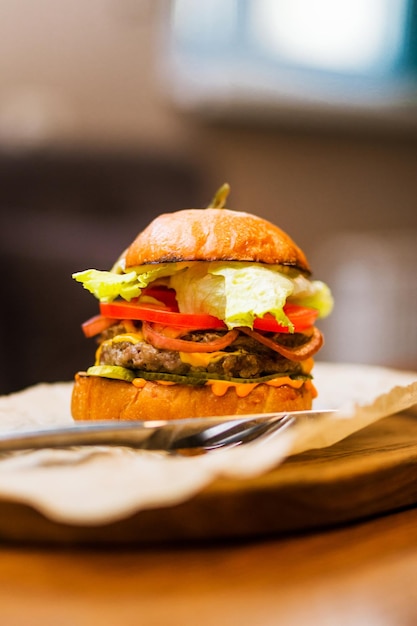 Le restaurant propose un burger au bœuf sauce fromage tomates fraîches et salade sur un plateau en bois Photo verticale