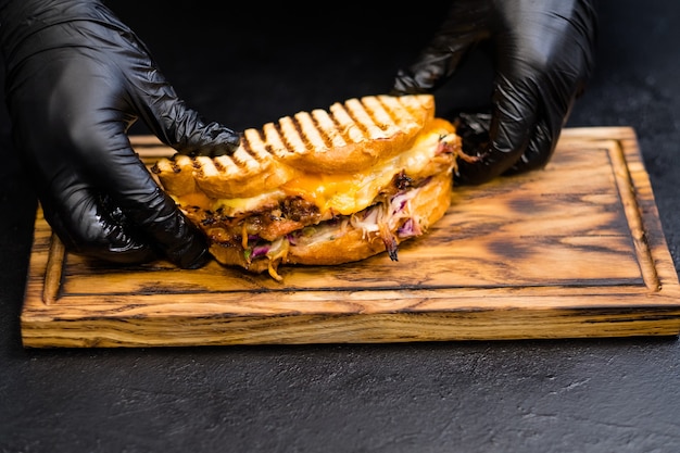 Restauration professionnelle. Les mains du chef servent un sandwich au porc effiloché avec du fromage sur une planche de bois.