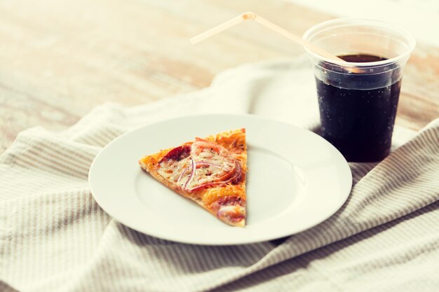 restauration rapide, cuisine italienne et concept de restauration - gros plan d'une tranche de pizza avec une tasse de coca cola sur une table en bois