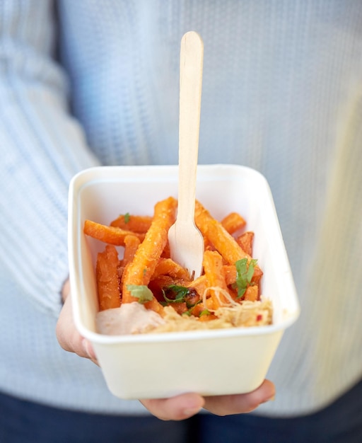 restauration rapide, personnes et concept de mauvaise alimentation - gros plan sur une main tenant une assiette jetable avec patate douce et fourchette