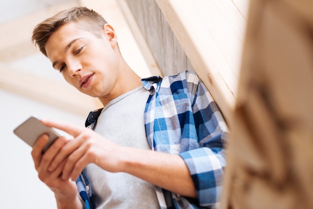 Rester en contact. Beau garçon élégant aux cheveux blonds concentré à l'aide de son téléphone et portant une chemise en tartan et en tapant un message