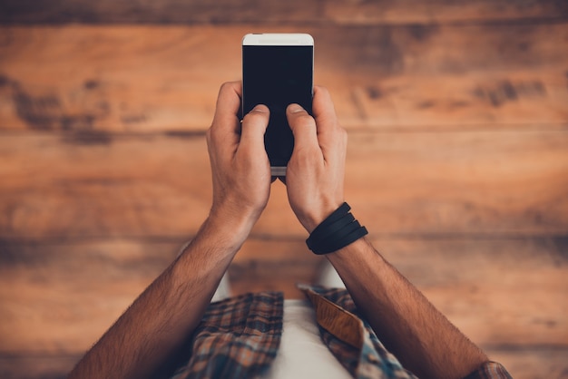 Rester en contact. Vue de dessus de l'homme tenant un téléphone intelligent en se tenant debout sur le plancher en bois