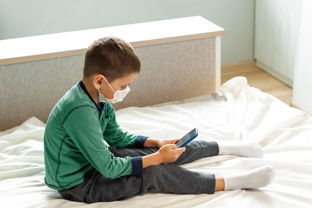 Rester à la maison, mettre en quarantaine la prévention de la pandémie de coronavirus. Un enfant ennuyé joue à la maison au téléphone pendant la quarantaine. Epidémie de prévention. COVID19.