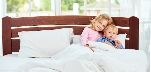 Rester à la maison mignon petit frère et soeur en pyjama et regarder la caméra avec le sourire