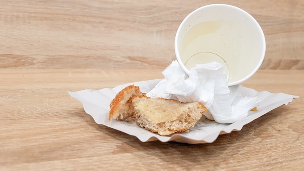 Les restes de nourriture sur une assiette en papier et une tasse de café en papier sale vide sur une table en bois dans un café de restauration rapide.