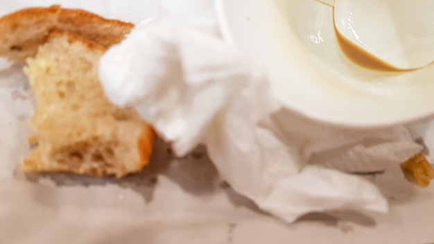 Les restes de nourriture sur une assiette en papier et une tasse de café en papier sale vide sur une table en bois dans un café de restauration rapide.