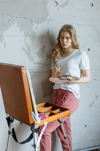 Restez à la maison: jeune fille avec pinceau et palette debout près de dessin de chevalet