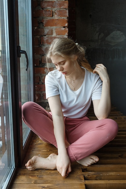 Restez à la maison: passer du temps dans l'ennui. jeune fille assise sur le rebord de la fenêtre