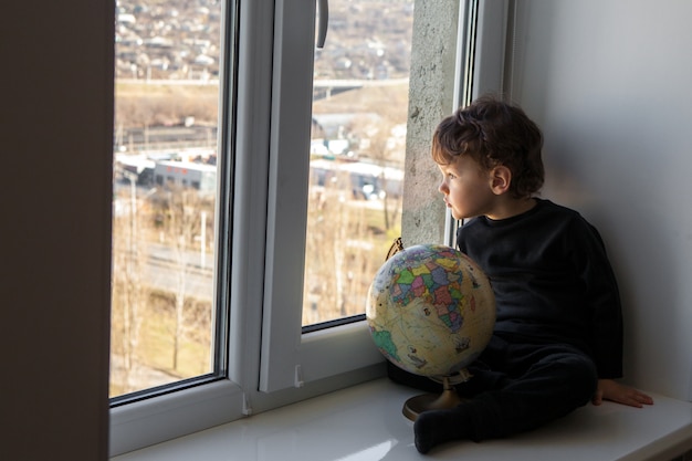 Restez positif à la maison. L'enfant est assis sur le rebord de la fenêtre et joue avec le globe