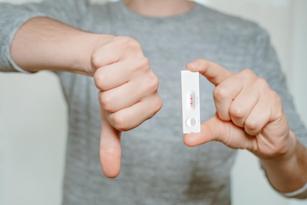 Photo résultat positif du test de coronavirus kit de test à domicile avec homme montrant le pouce vers le bas - restez à la maison