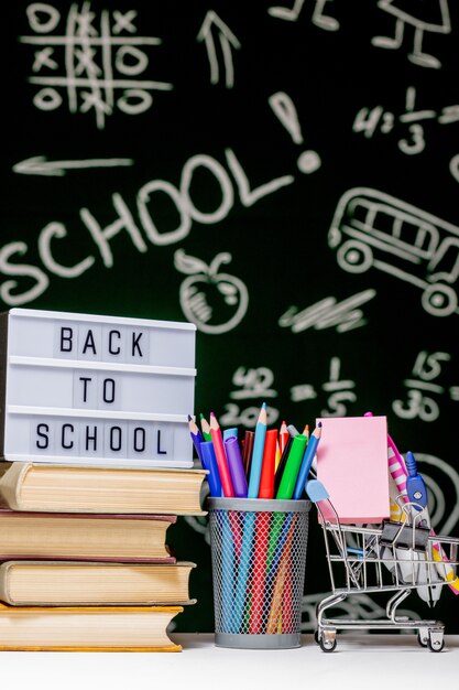 Retour à l'arrière-plan de l'école avec des livres, des crayons et un globe sur tableau blanc sur un fond de tableau noir vert.