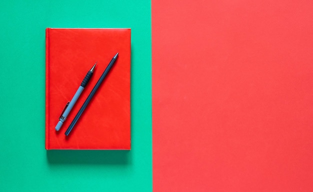 Retour au concept de l'école. Bloc-notes rouge avec des crayons. Fond vert et rouge. Mise à plat avec espace de copie. Automne