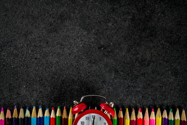 Retour au concept de l'école avec des livres crayons de couleur réveil fond tableau noir