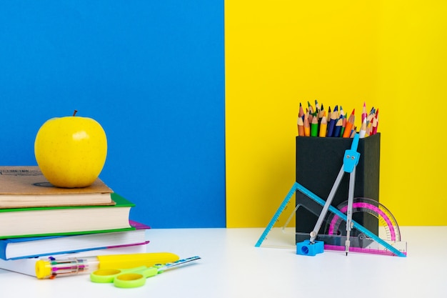 Retour à la disposition de l'école avec des livres, des crayons et des pommes sur un tableau blanc, un mur bleu et jaune, le concept de l'école