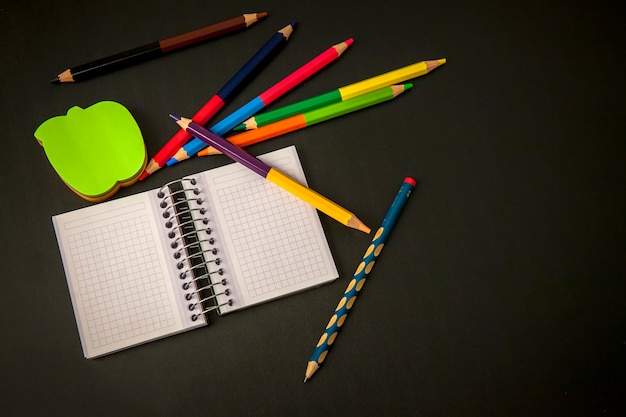 Retour à l'école: cahier avec un crayon et des crayons de couleur sur un tableau noir