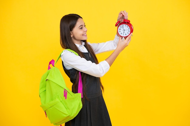 Retour à l'école Écolière adolescente avec sac à dos tenir l'heure du réveil pour apprendre Écoliers sur fond jaune isolé Bonne fille face à des émotions positives et souriantes