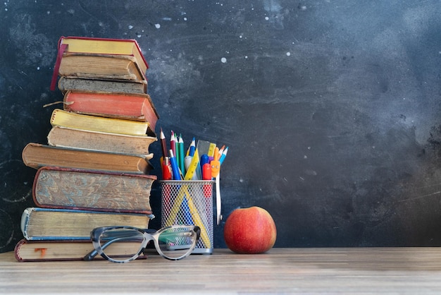 Retour à l'école concept fournitures scolaires colorées avec des livres et pomme rouge sur étagère fond de tableau noir avec espace de copie