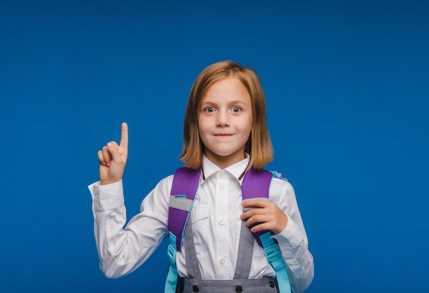 Retour à l'école écolière positive mignonne en uniforme leva le doigt posant sur un fond bleu Préparation pour l'école une idée intéressante Espace pour la copie