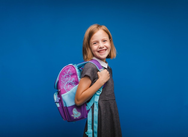 Retour à l'école Une écolière avec un sac d'école sur un fond de studio bleu isolé une petite fille tient un sac à dos