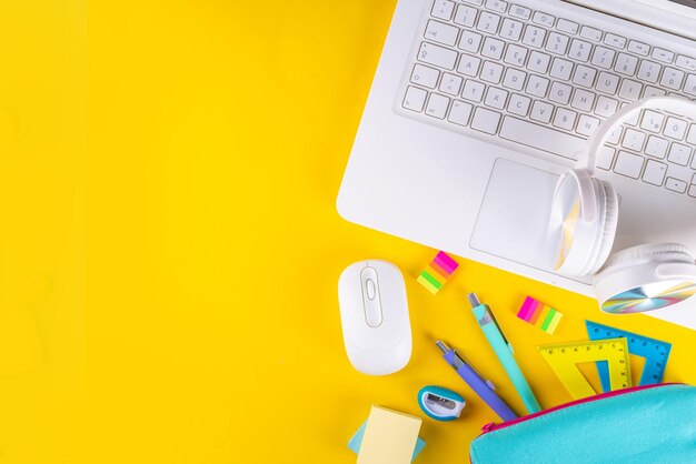Retour à l'école éducation en ligne fond jaune vif coloré ordinateur portable blanc avec fournitures scolaires casque étui à crayons et accessoires vue de dessus espace de copie à plat