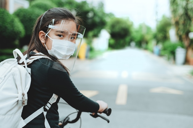 Retour à l'école. enfant asiatique fille portant un masque facial avec sac à dos faire du vélo et aller à l'école. pandémie de coronavirus.Nouveau mode de vie normal.Concept d'éducation.